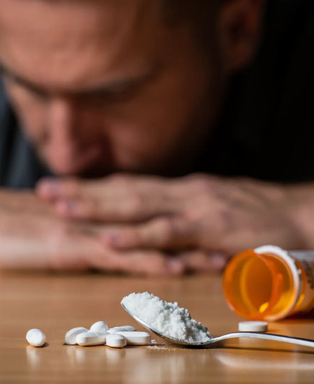 Наркотическая зависимость Таблетки и порошок на столе перед мужчиной